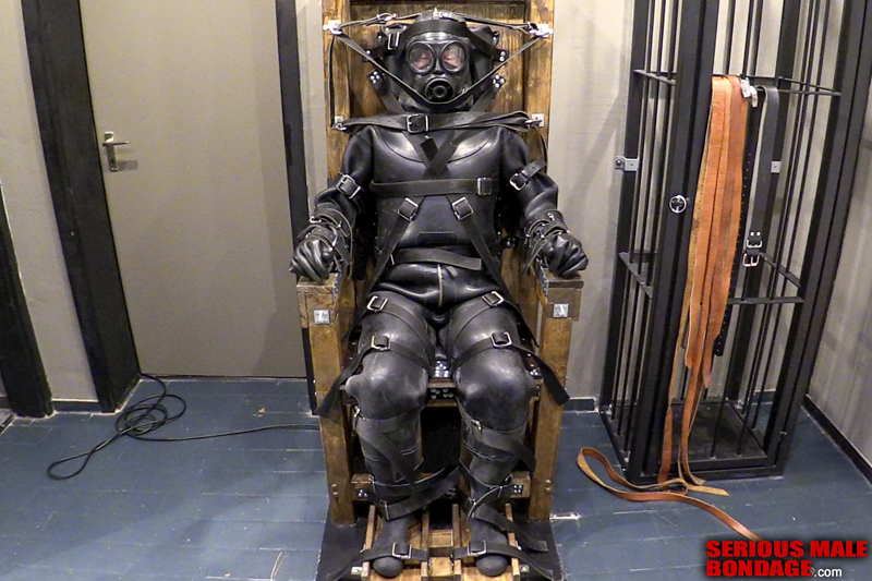 Mark is restrained in a rubber suit and bondage chair
