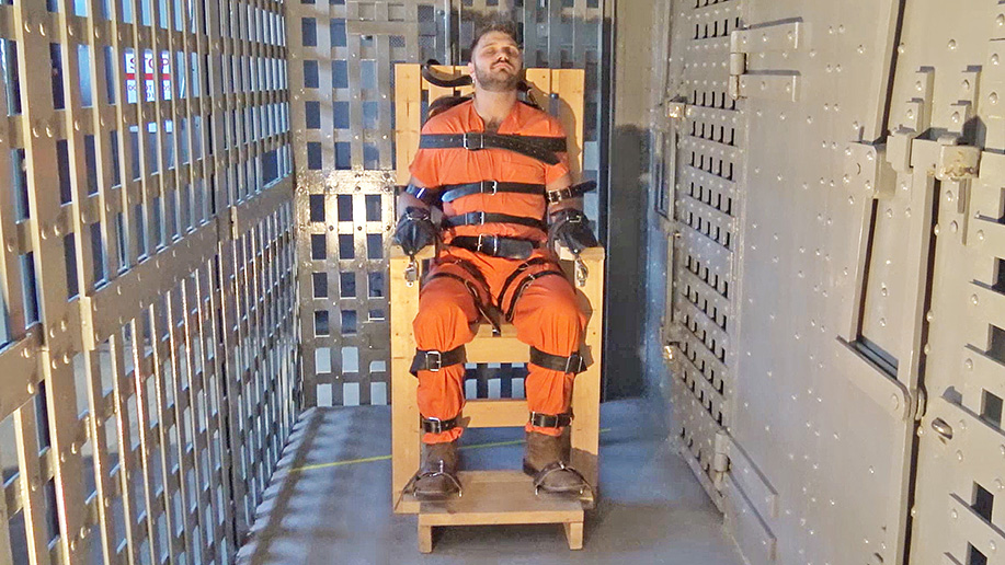 Hooded and strapped inescapably in a bondage chair